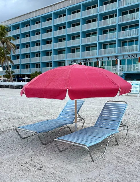 Two beach lounge chairs under a pink umbrella on the sand in front of Lani Kai Island Resort.