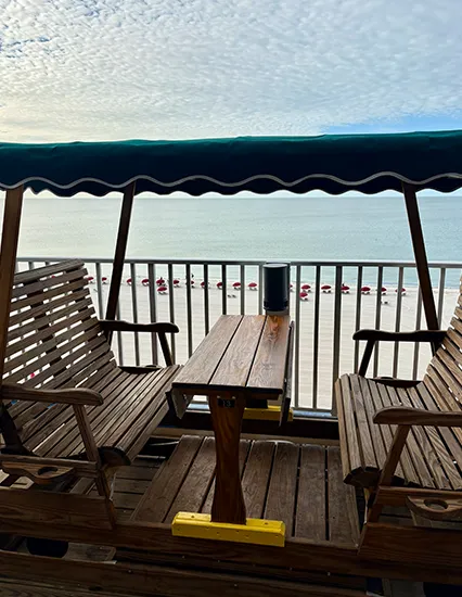 Shaded wooden swing seating with table on the Sundeck overlooking Fort Myers Beach and the Gulf of Mexico.