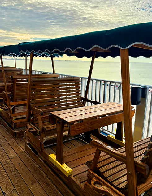 Wooden swing seating with tables on the Sundeck overlooking calm Gulf of Mexico waters at Lani Kai Island Resort.
