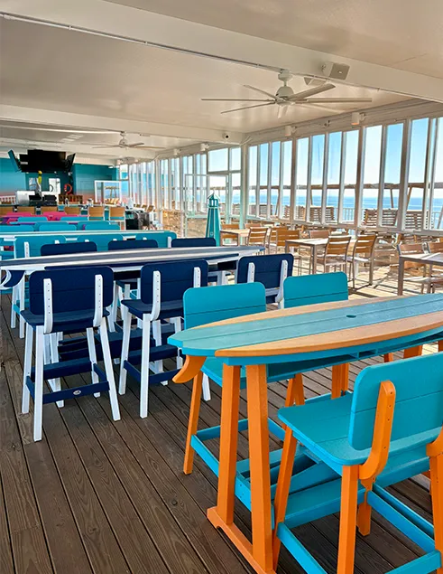 Colorful open-air rooftop dining at the Sundeck with ocean views, long communal tables, and coastal décor at Lani Kai Island Resort.